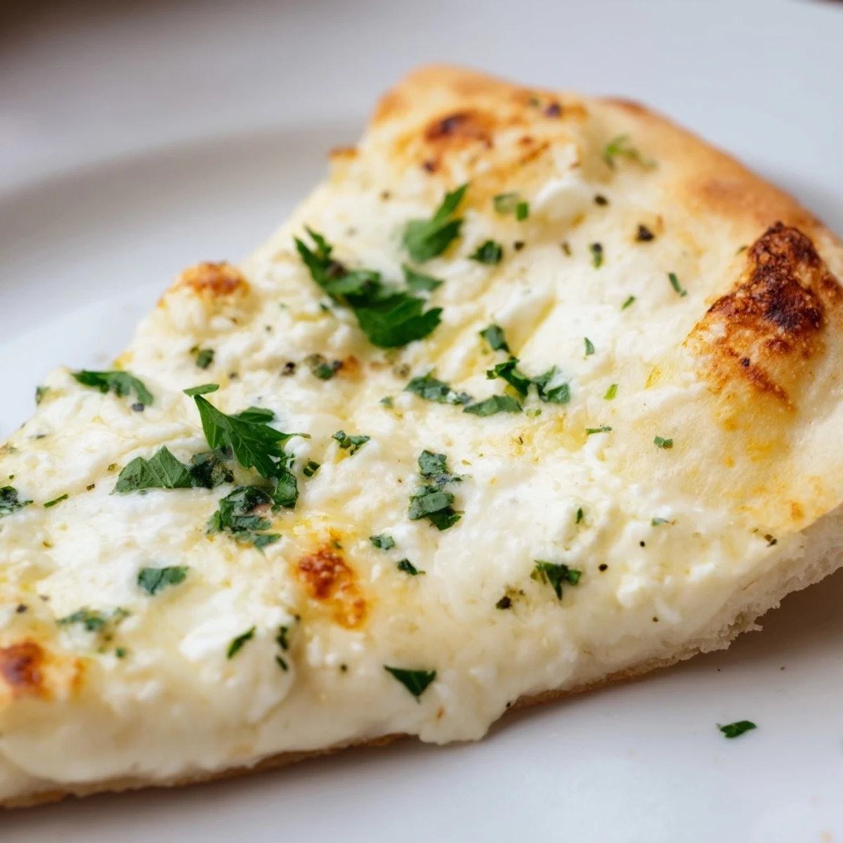 A close-up view shows a slice of Creamy Garlic White Pizza, featuring its creamy white sauce and melted cheese topping the golden-brown crust.