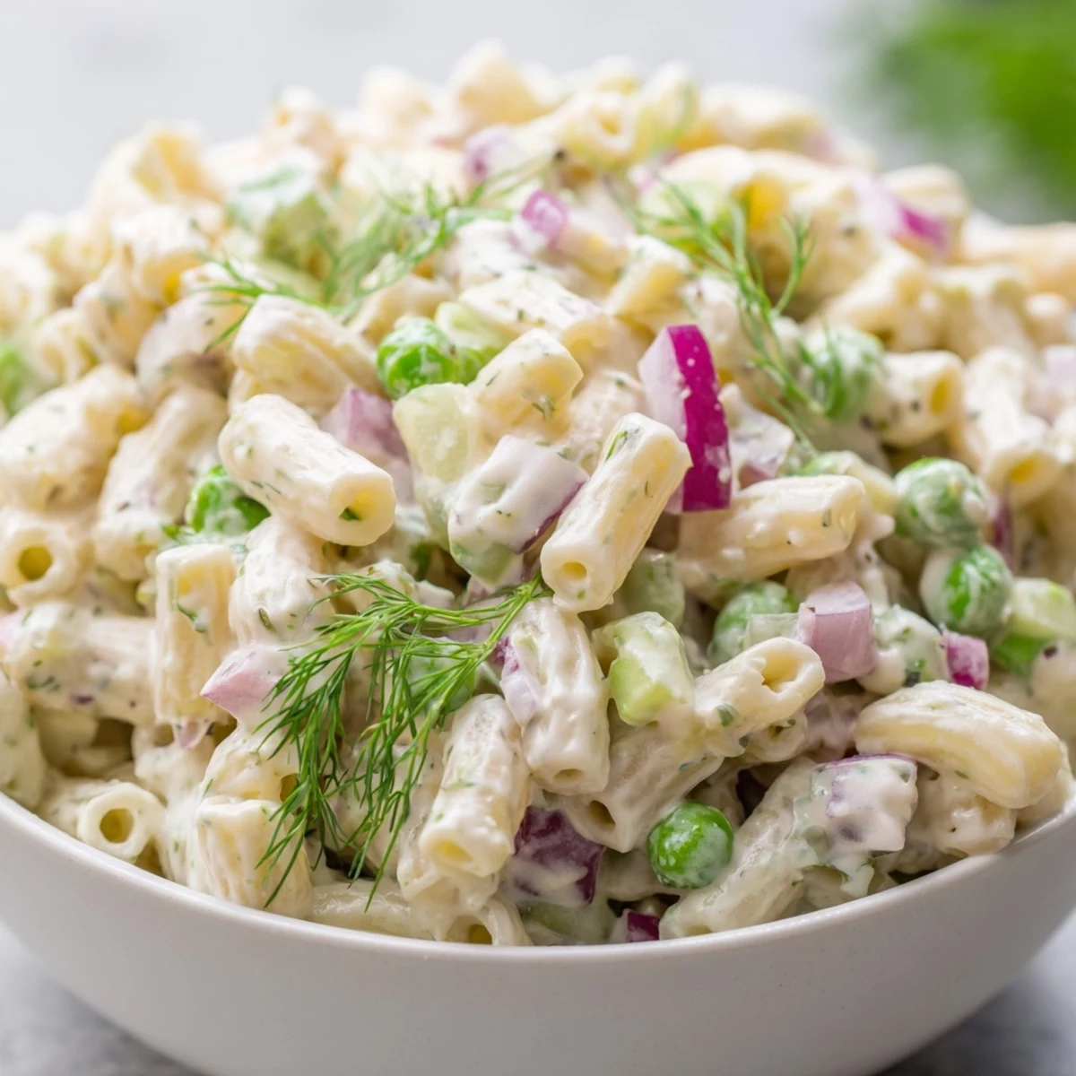 Chilled dill pickle pasta salad in a serving dish, featuring crunchy pickles and peas in creamy dressing.