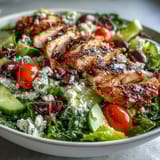 A refreshing Greek salad bowl with tender grilled chicken, colorful vegetables, and tangy Kalamata olives, drizzled with zesty lemon-oregano dressing.  