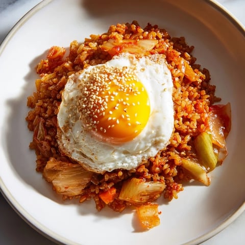 Steaming hot bowl of kimchi fried rice topped with a golden fried egg and sesame seeds.