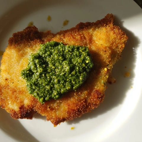 Golden, crispy panko-crusted chicken cutlets topped with vibrant green basil pesto and fresh herbs on a white plate.  