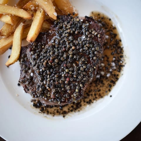 A close-up image showcases the rich peppercorn crust on the ribeye, served with delicious fries.