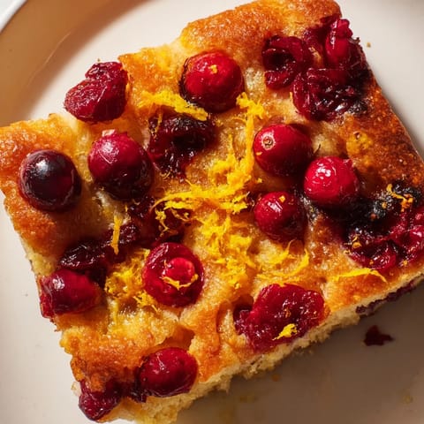 A close-up of a rustic, bubbly Cranberry Orange Focaccia ready to slice and enjoy as a treat.
