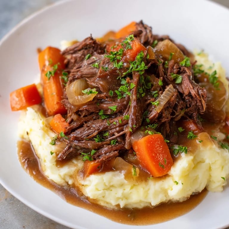 A steaming plate of slow cooker pot roast, rich gravy over flavorful mashed potatoes.