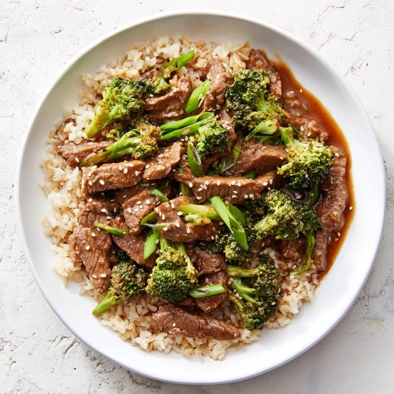Warm bowl of Slow-Cooker Beef & Broccoli served over fluffy brown rice and fresh mixed greens.