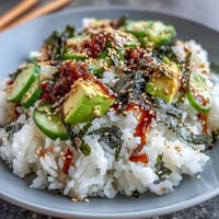 A vibrant sushi bowl with seasoned rice, crisp cucumber, creamy avocado, and nori strips, drizzled with spicy mayo for a satisfying meal.