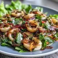 A colorful chilli-lime squid salad with tender rings, fresh herbs, and crisp vegetables in a tangy dressing.